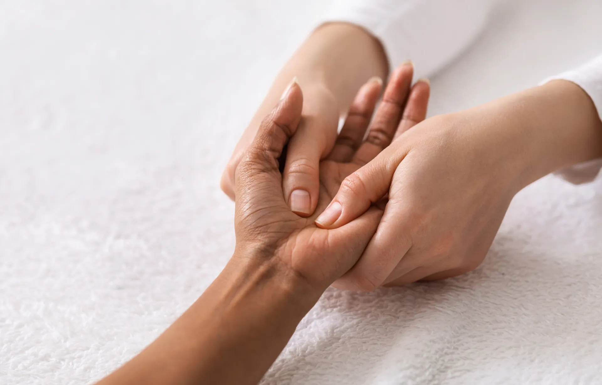Handmassage: Zwei Hände bei einer Reflexzonenbehandlung über einem weißen Handtuch