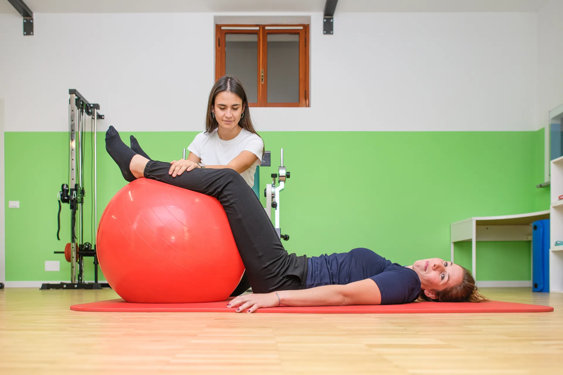 Therapeutin begleitet eine Übung auf einem großen Gymnastikball